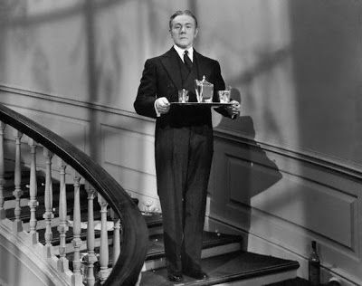 a man in a suit and tie holding a tray with chess pieces on it while standing at the top of stairs