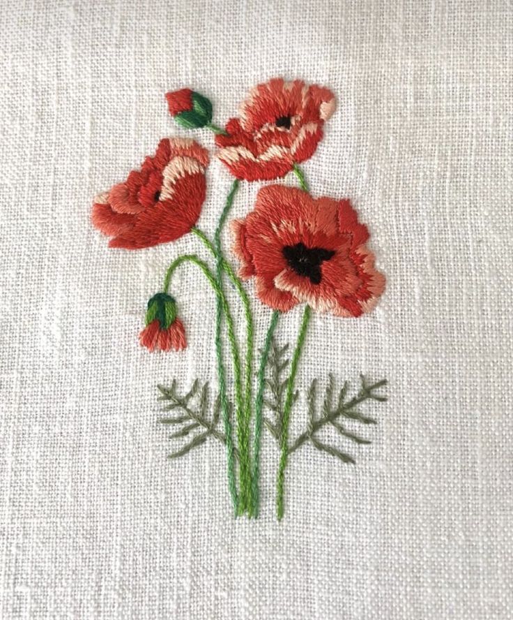 some red flowers are on a white linen material with green stems and leaves in the center