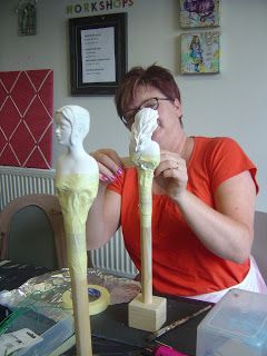 a woman sitting at a table with two wooden mannequins in front of her