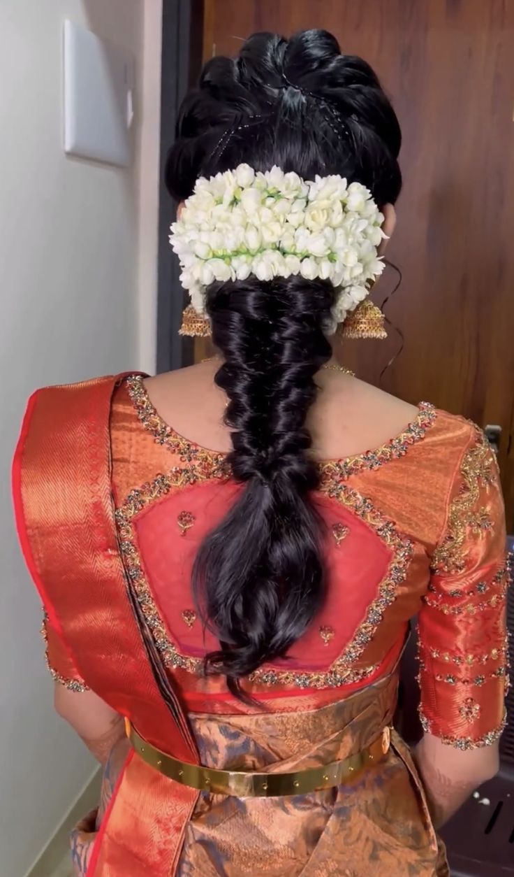 a woman with flowers in her hair wearing an orange and gold sari dress,