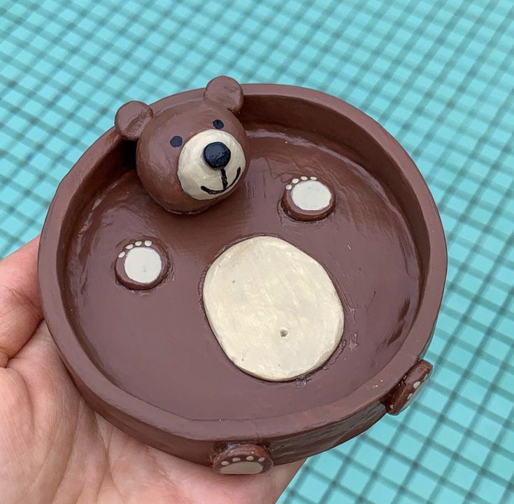 a hand holding a chocolate bear shaped cake in the shape of a pool with blue water