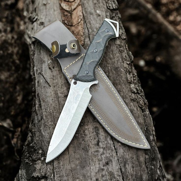 a knife that is laying on top of a piece of wood next to a tree