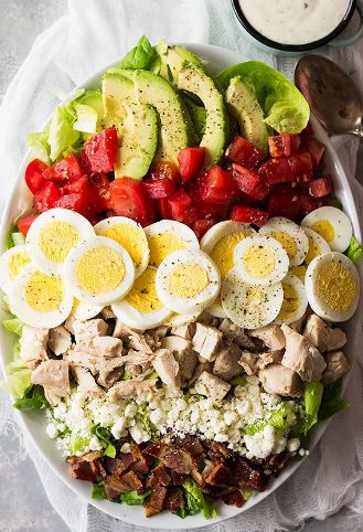 a salad with hard boiled eggs, tomatoes, lettuce and bacon on it