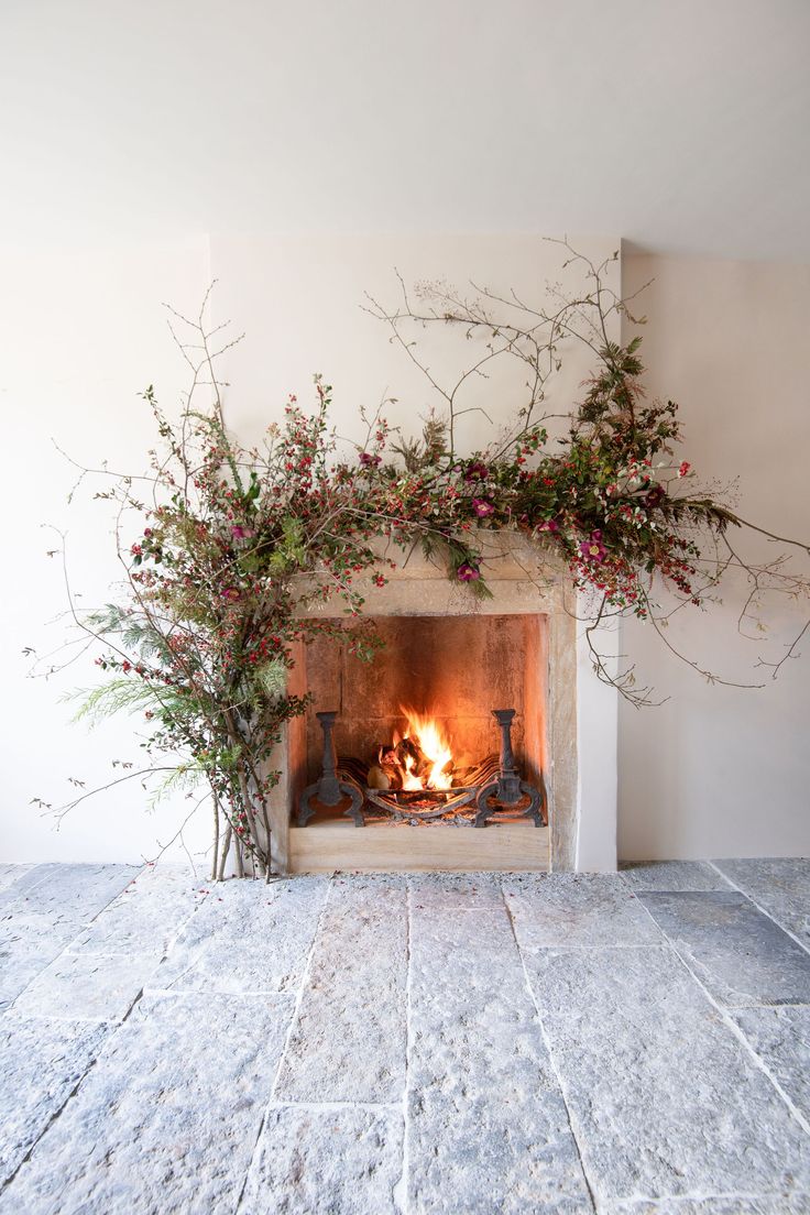 the fireplace is decorated with greenery and flowers on it's mantle, along with an open fire