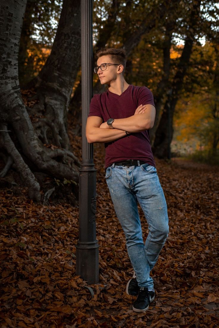 a young man leaning against a street lamp in the fall leaves with his arms crossed