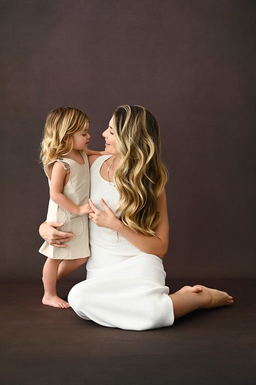 a mother and her daughter sitting on the floor with their arms around each other looking at each other