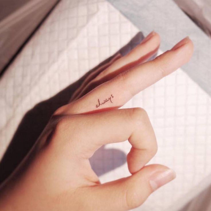 a woman's hand with a small tattoo on her left thumb and the word joy written in cursive writing