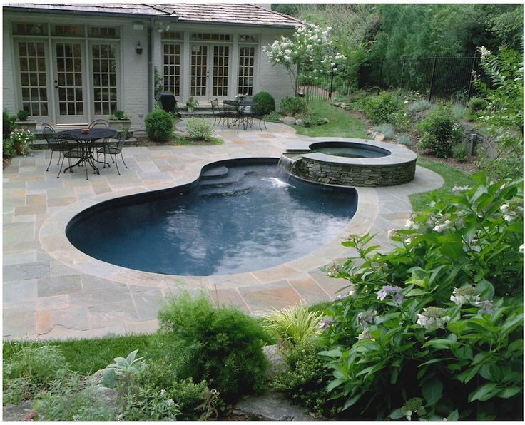 a backyard with a swimming pool and patio furniture in the back yard, surrounded by greenery