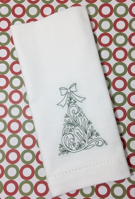 a white towel with a christmas tree embroidered on the front and green, red, and white circles around it