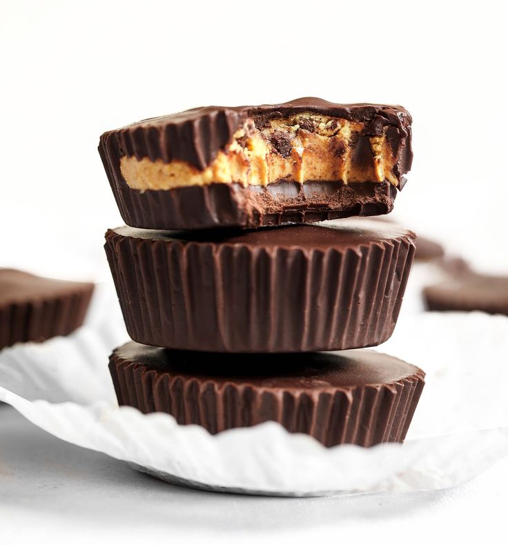 three chocolate cups stacked on top of each other with peanut butter in the middle and text overlay reading cookie doughnut protein cups