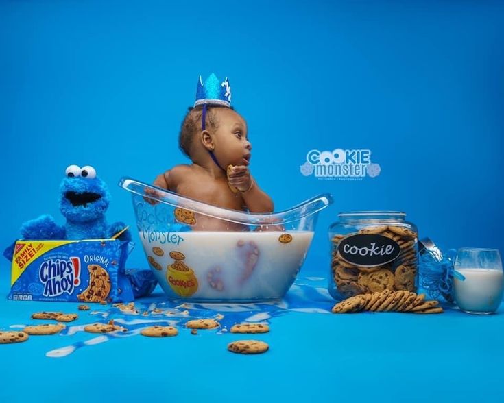 a baby sitting in a bowl surrounded by cookies and milk