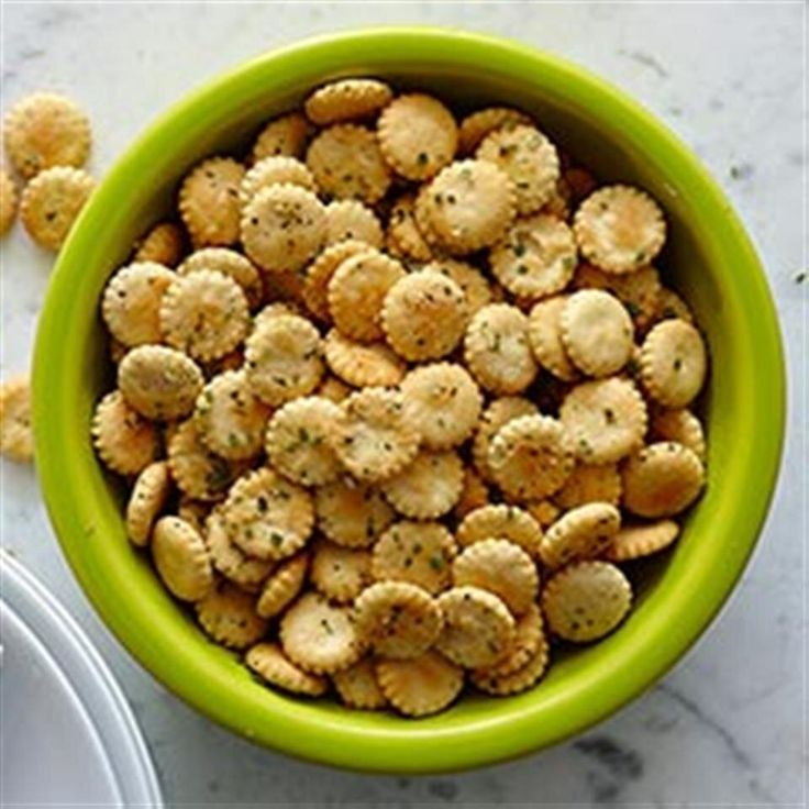 a green bowl filled with small crackers on top of a white counter next to a plate