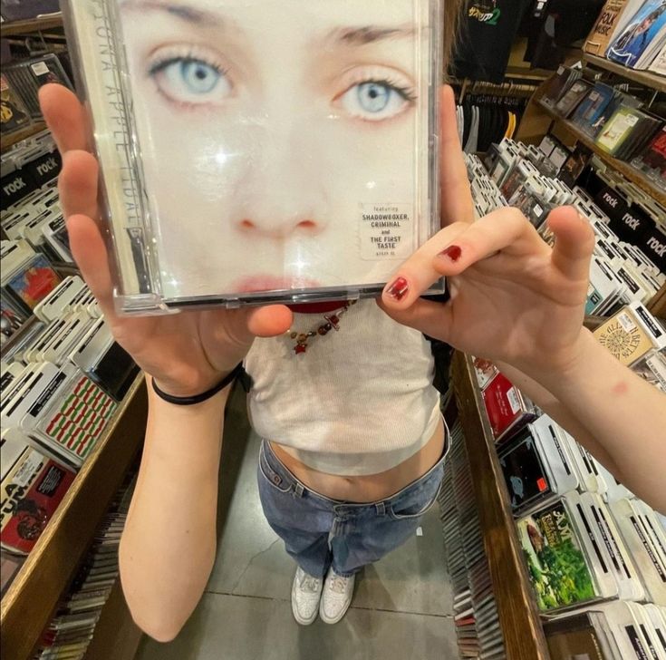 a woman holding up a cd in front of her face with the cover pulled back