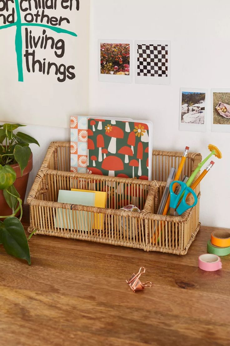 a wooden desk topped with lots of office supplies next to a potted green plant