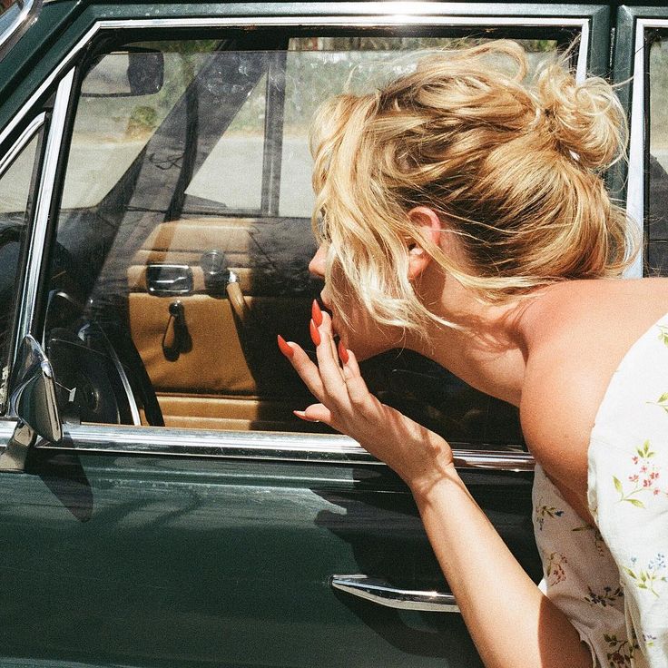 a woman leaning out the window of a green car with her hand on her face