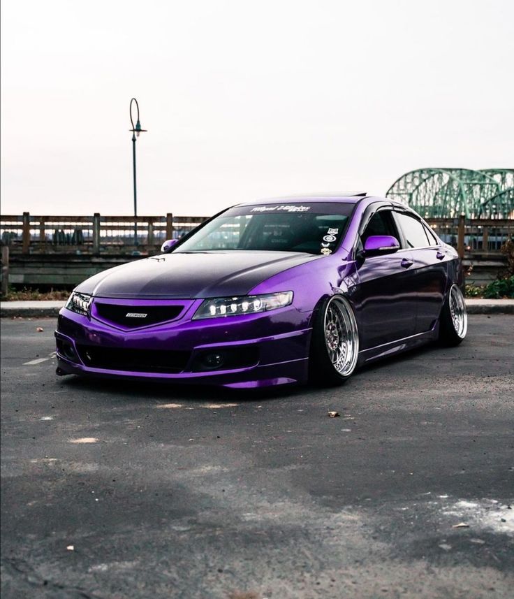 a purple car parked in a parking lot next to a green and white bridge on a cloudy day