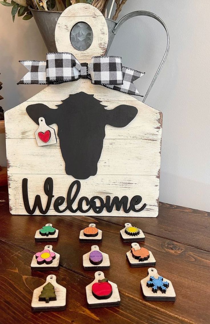 a wooden welcome sign sitting on top of a table next to small magnets and a potted plant