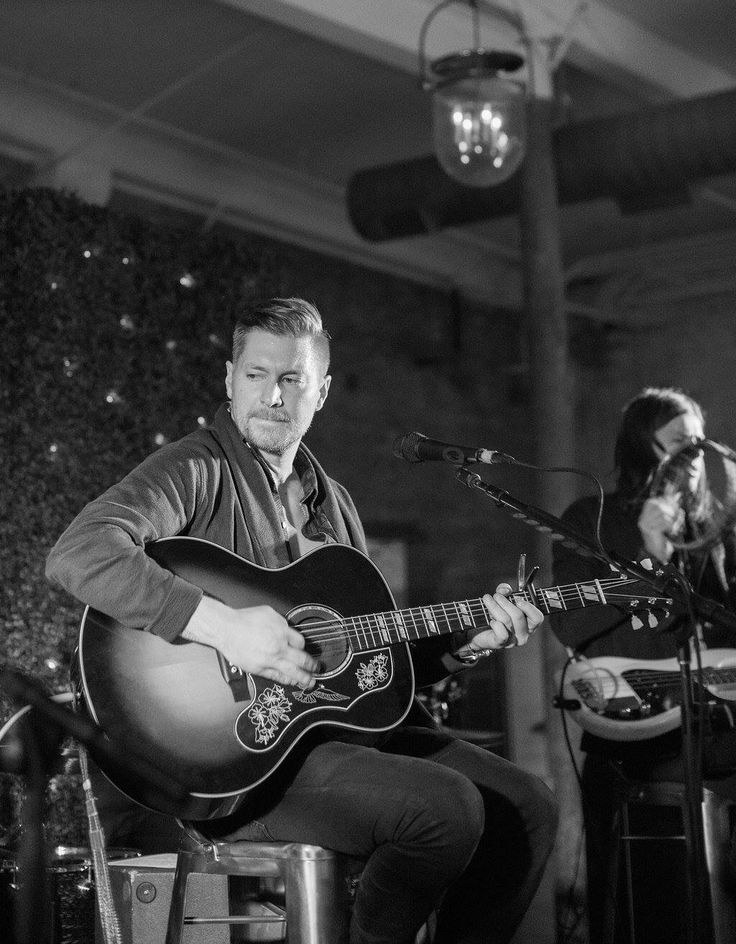 two people are playing guitars and singing into microphones while another person sits in the background