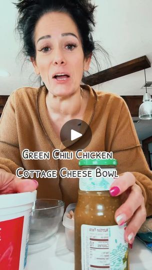 a woman sitting at a table with two jars of green chili chicken cottage cheese bowl