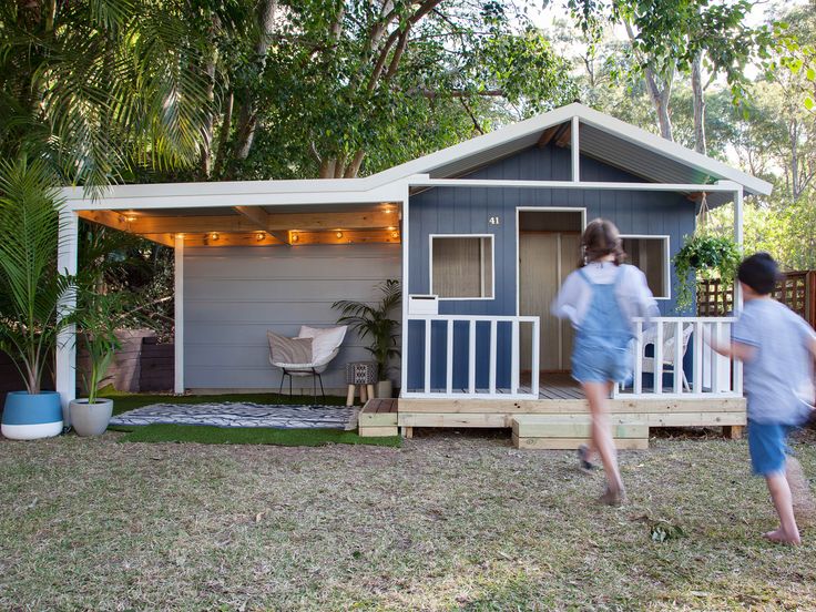 two people are walking towards a tiny house with lights on the porch and door open