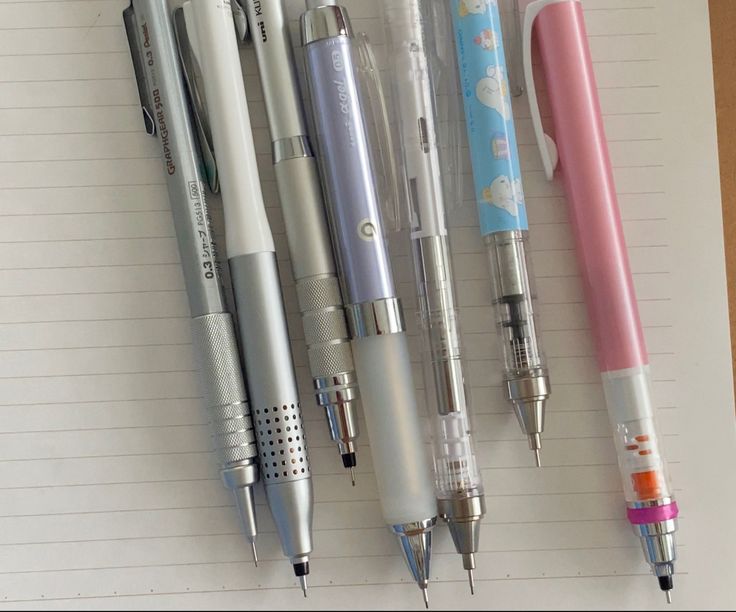 several pens lined up on top of each other in a row next to an open notebook