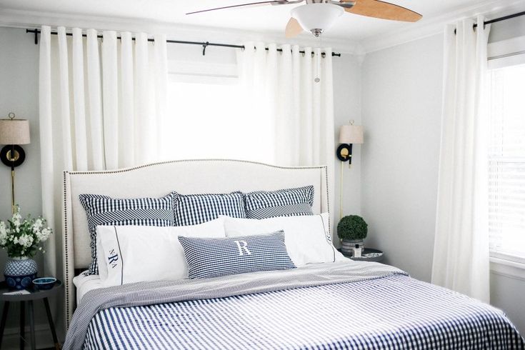 a bedroom with white and blue bedding, windows, and a ceiling fan in the corner