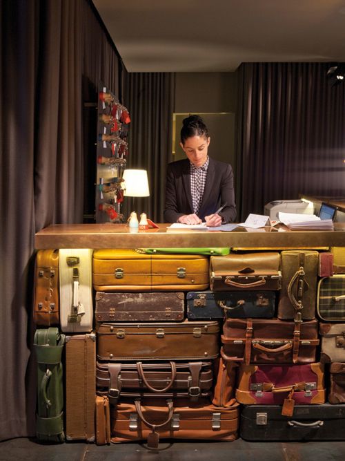 a man sitting at a desk with lots of suitcases stacked on top of it