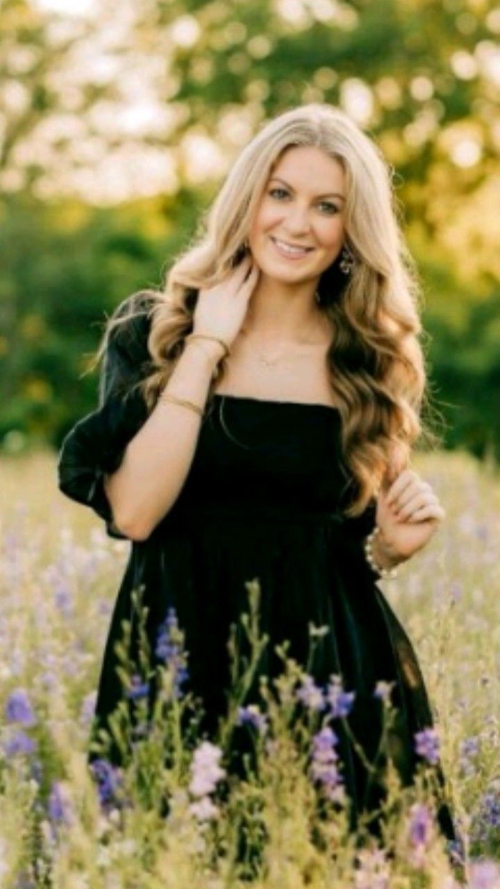 a woman standing in the middle of a field with long hair and wearing a black dress