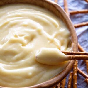 a wooden bowl filled with white sauce on top of a blue table cloth next to pretzels