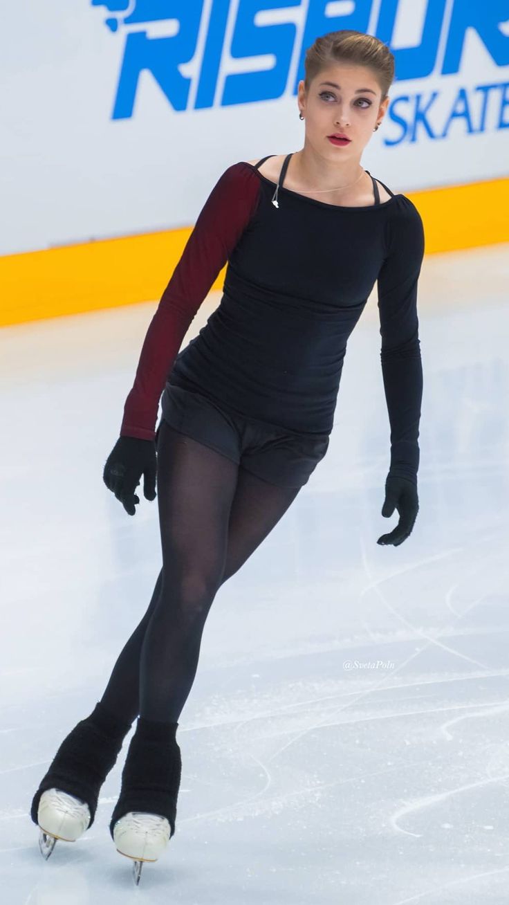 a woman skating on an ice rink wearing black tights and holding her leg in the air