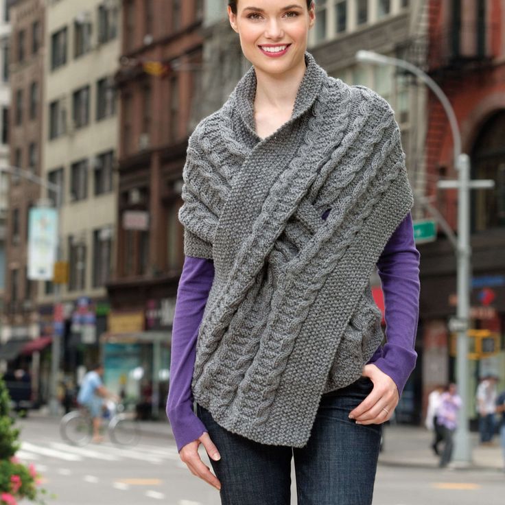 a woman standing in the street wearing a gray knitted shawl and purple shirt