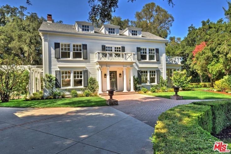 a large white house with lots of windows and bushes in front of the entrance to it