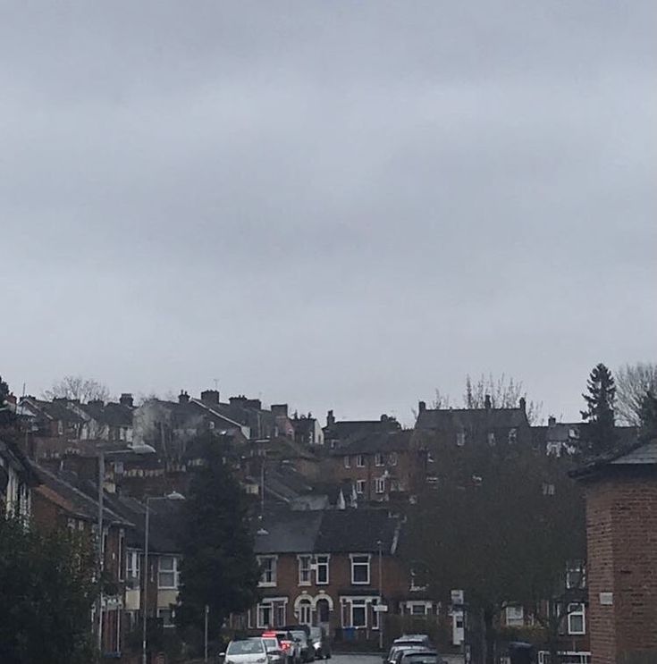 cars are parked on the street in front of some houses and buildings under a cloudy sky