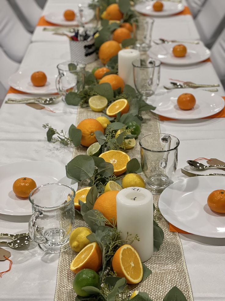 a long table is set with oranges and greenery for a festive centerpiece