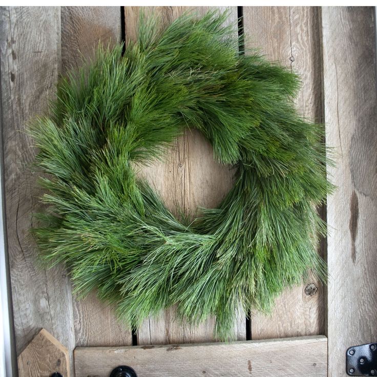 a wreath is hanging on the front door with two black knobs and one has green needles