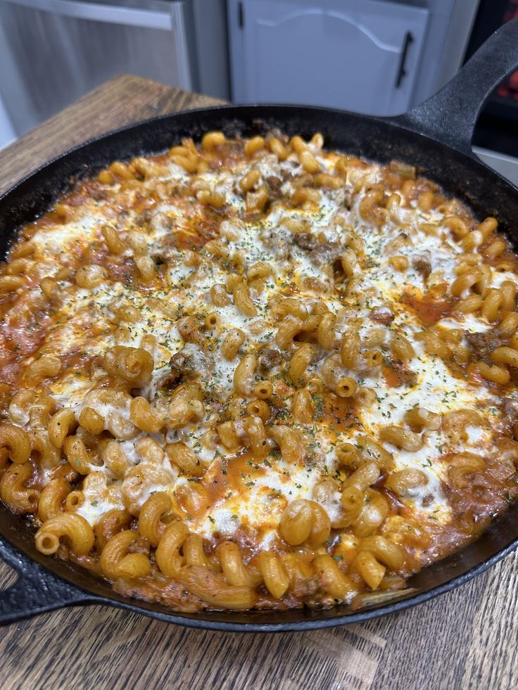 a skillet filled with macaroni and cheese on top of a wooden table