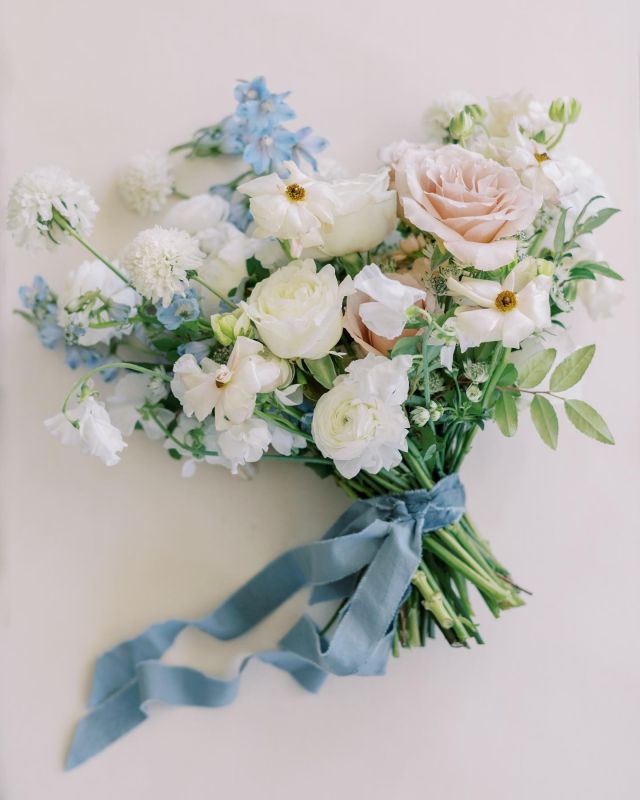 a bouquet of white and blue flowers is tied with a light blue ribbon on a white surface