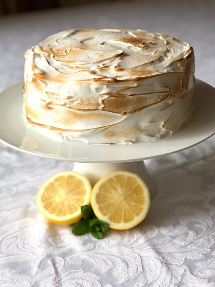 a cake with frosting and lemon slices on a white tablecloth next to two sliced lemons