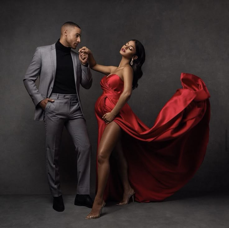 a man standing next to a woman in a red dress on a gray background with her legs spread out