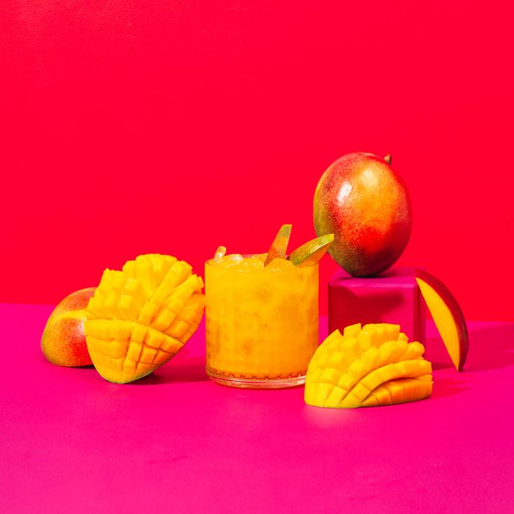 an orange smoothie with mangoes and apples on a pink background, surrounded by other fruit