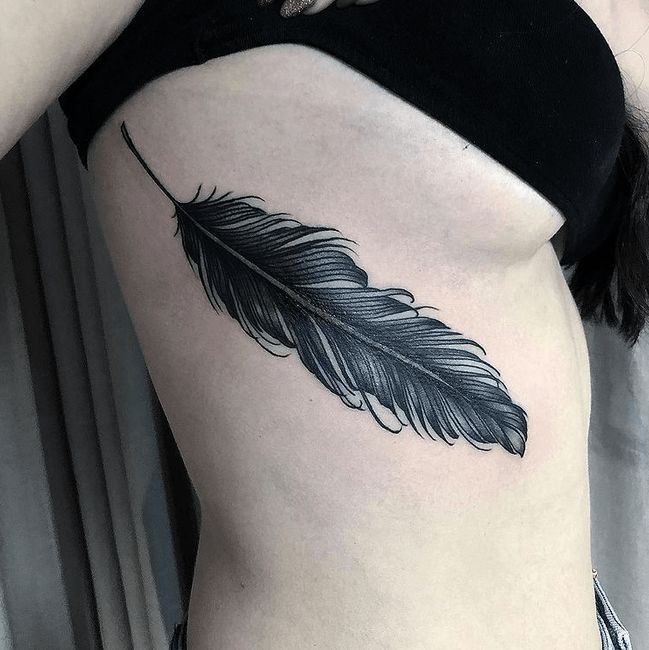 a woman's stomach with a black feather tattoo on it