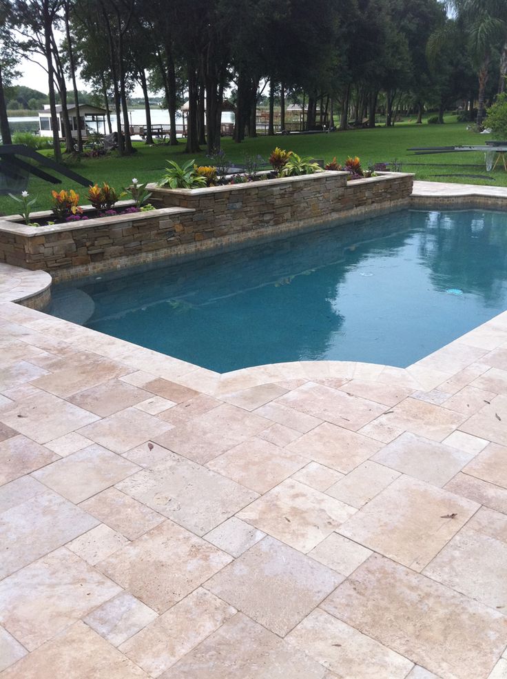 an empty swimming pool surrounded by stone steps and landscaping area with trees in the background