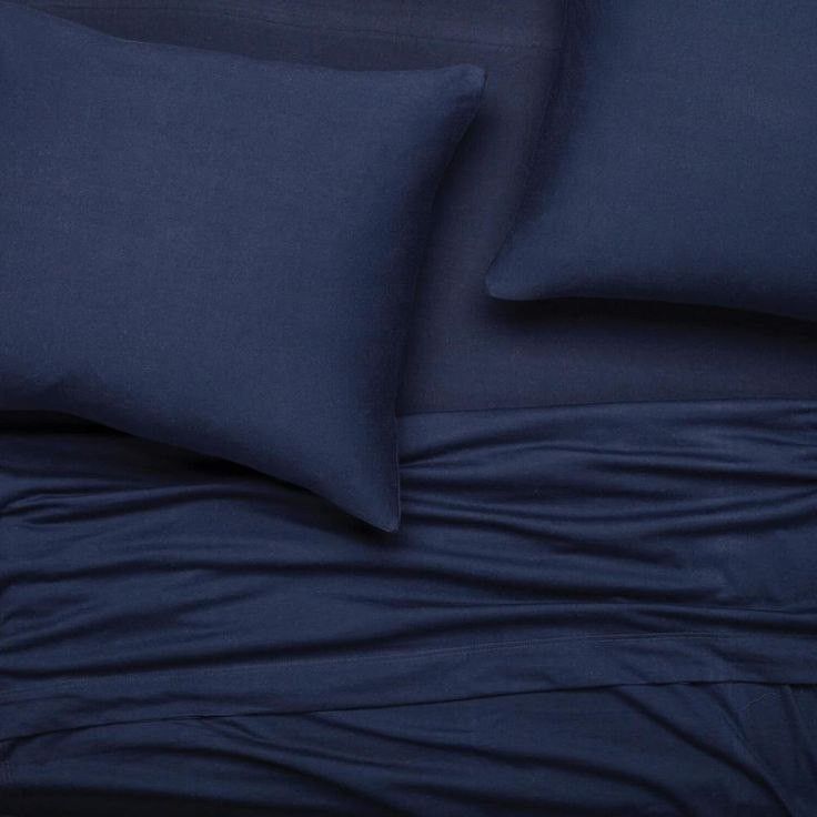 a bed with blue sheets and pillows on top of it, next to a pillow case