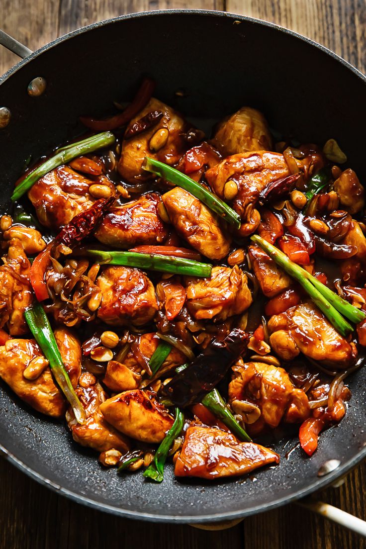 a pan filled with chicken and vegetables on top of a wooden table next to chopsticks