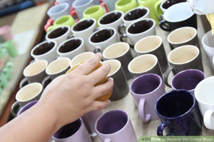 a person is holding a cup in front of many coffee mugs on a table