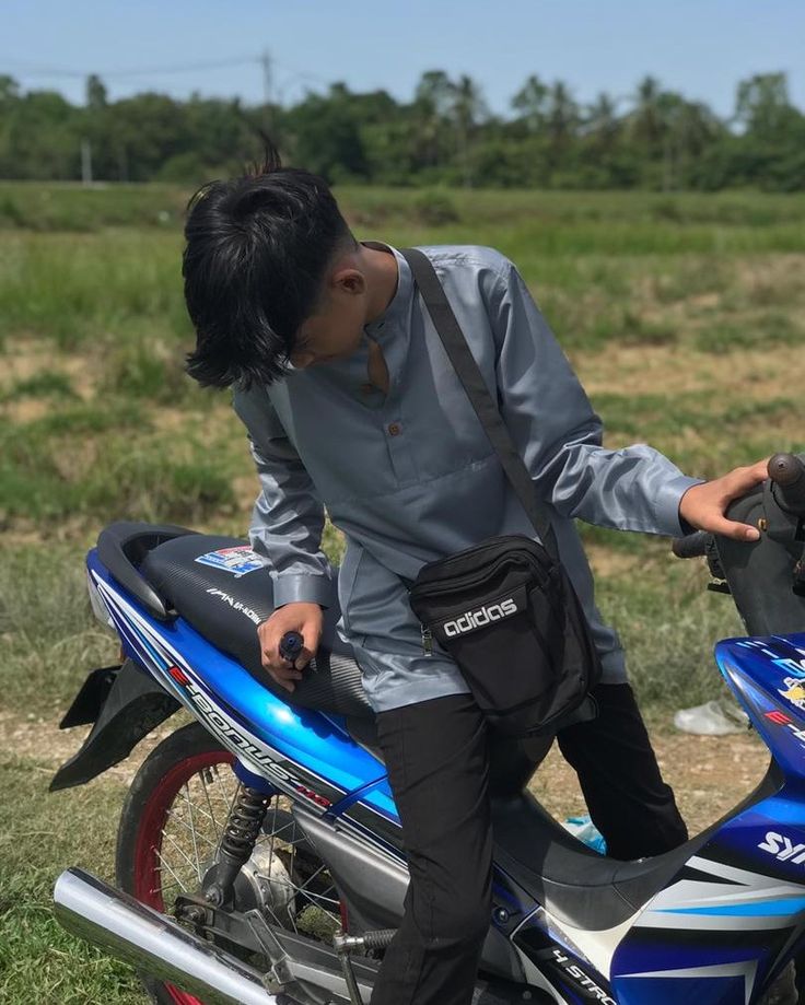 a man sitting on top of a blue and silver motorcycle in a field with grass