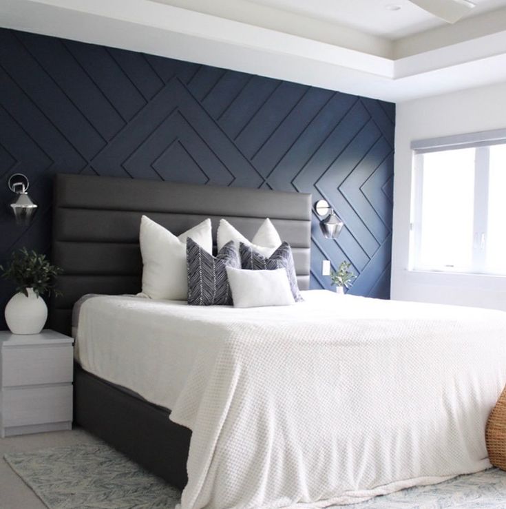 a bed with white sheets and pillows in a room that has dark blue accent walls