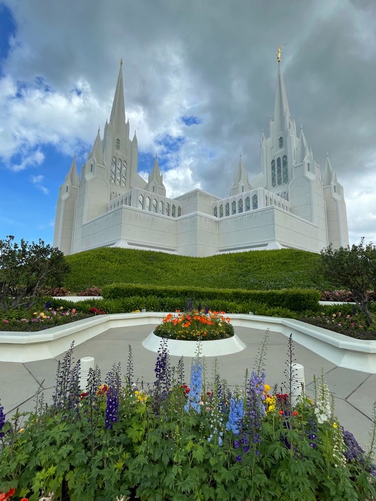 a large white building sitting on top of a lush green hillside next to flowers and bushes