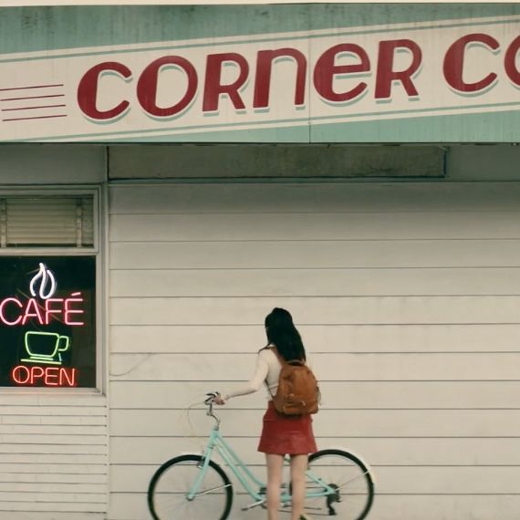 a woman standing next to a bike in front of a coffee shop