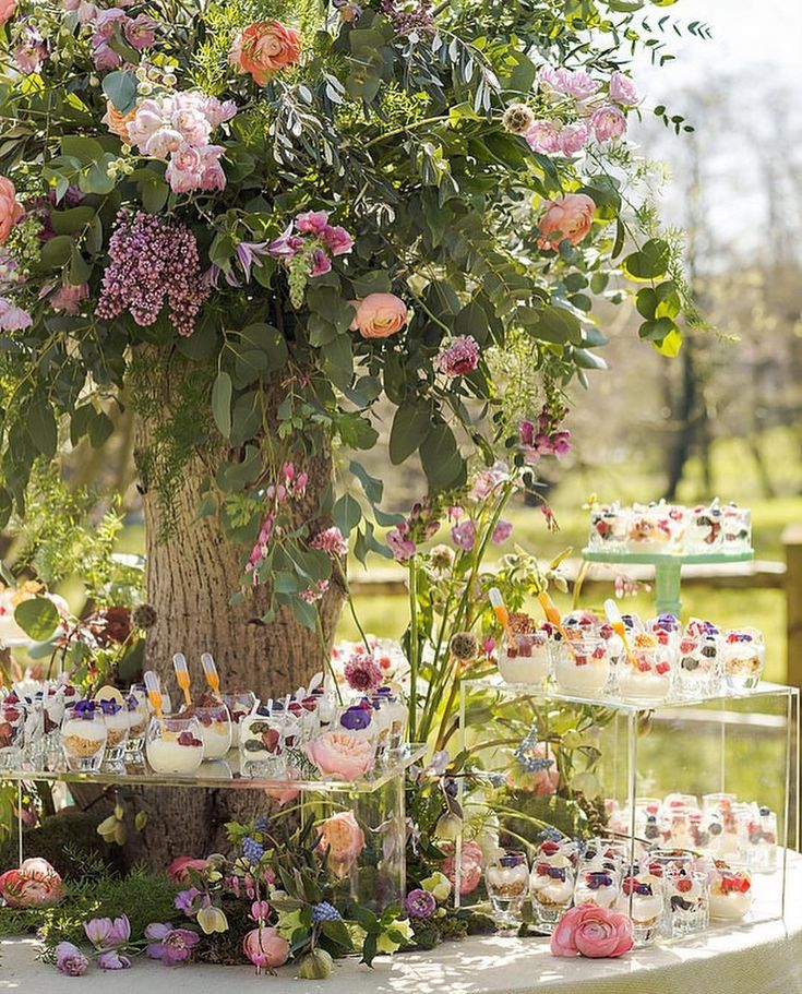 a table topped with cakes and cupcakes next to a tree filled with flowers